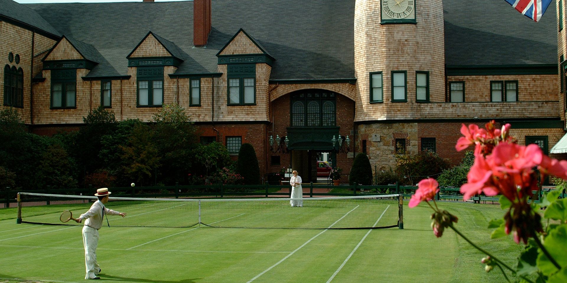 A Group Of People On A Grass Court With International Tennis Hall Of Fame In The Background